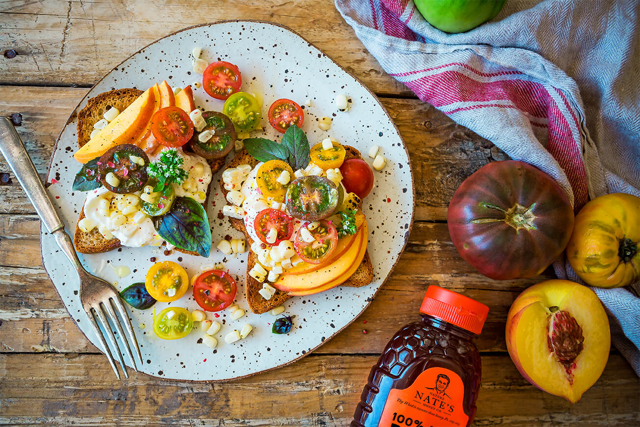 Open-faced sandwich with burrata, heirloom tomatoes, peaches and basil, with Nate's honey bottle on the side.
