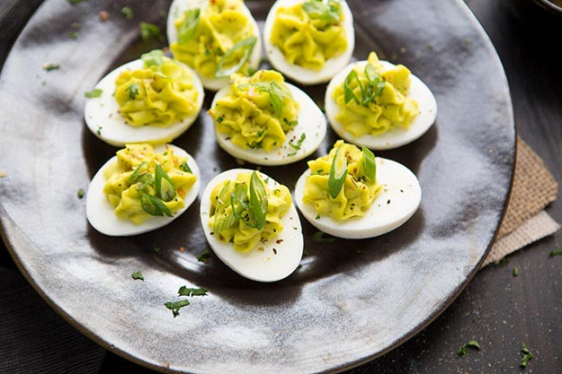 Deviled eggs garnished with chives on a textured dark plate.
