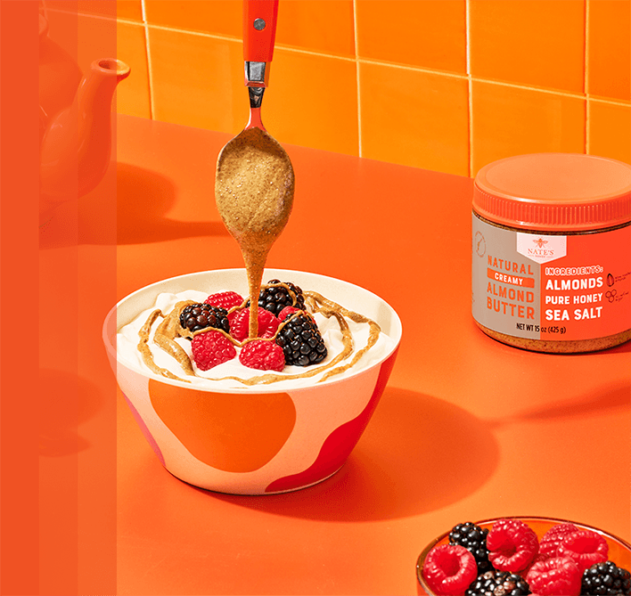 Almond butter drizzled from a spoon into a bowl of yogurt topped berries.