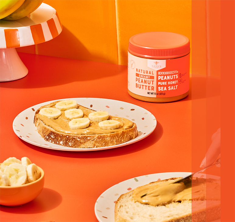 Toast topped with peanut butter and banana slices on an orange background, with a jar of peanut butter nearby.