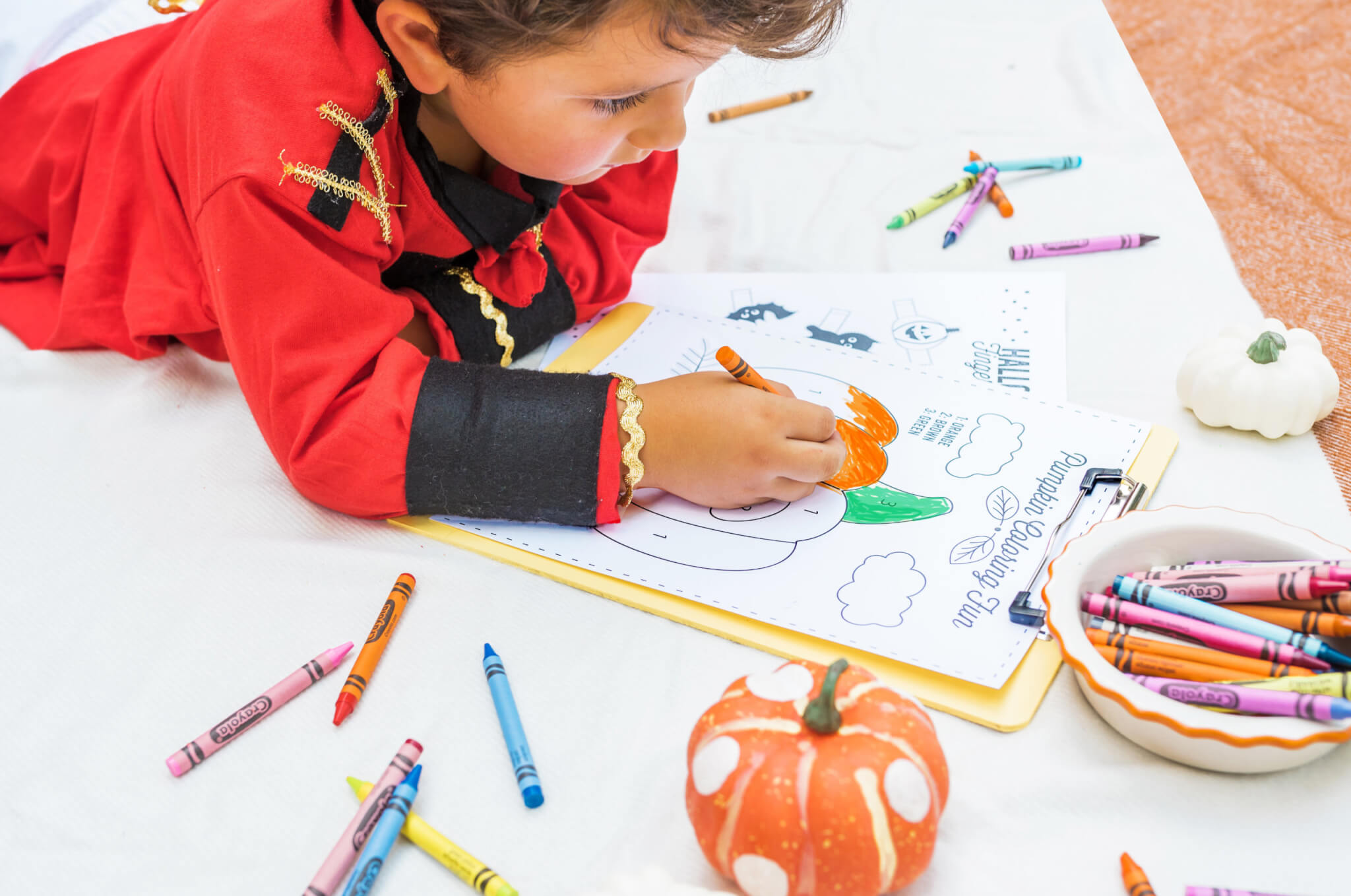 A child focused on coloring a Halloween-themed activity sheet surrounded by scattered crayons on the floor.