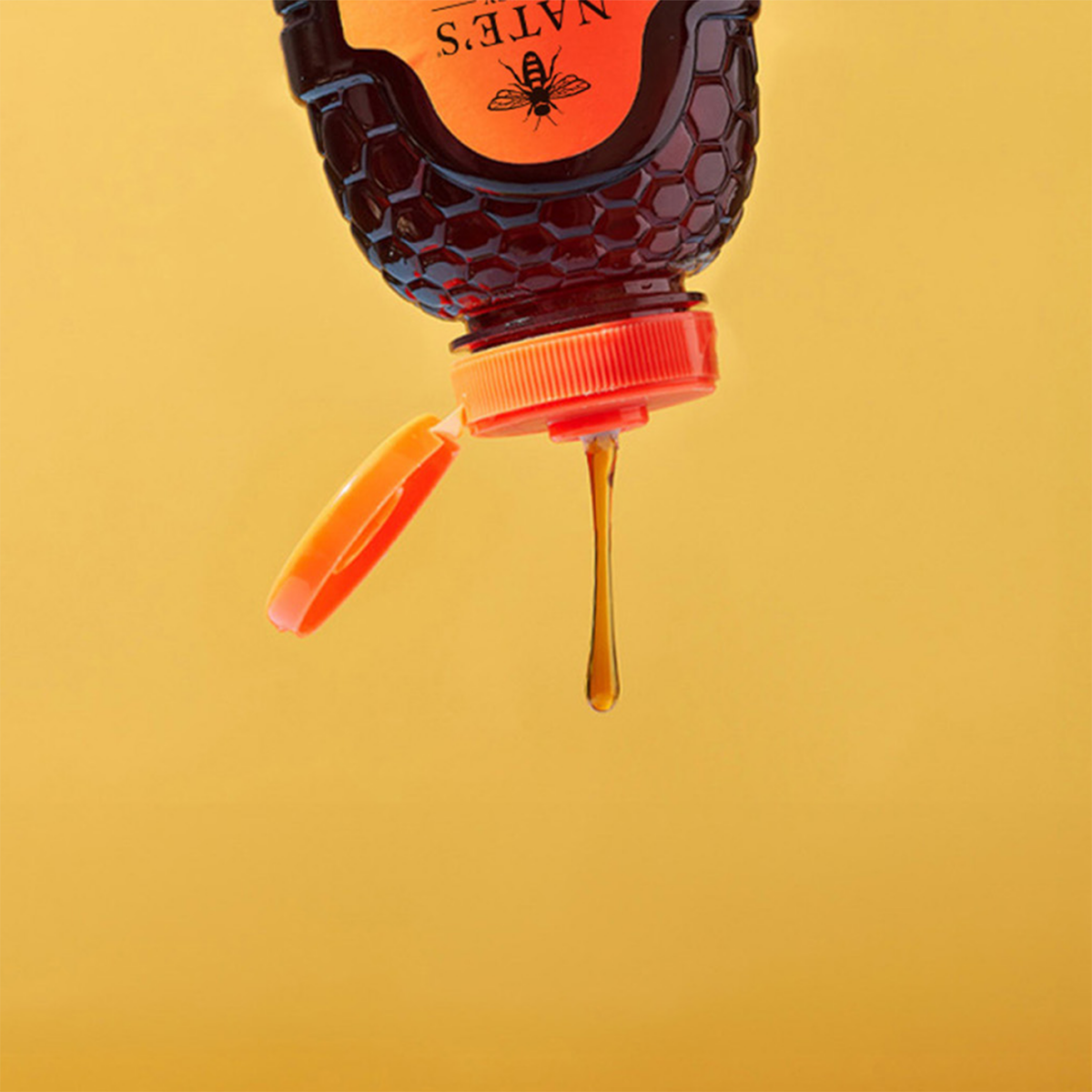 Drip of Nate’s Honey falling from a squeeze bottle against a warm yellow background.