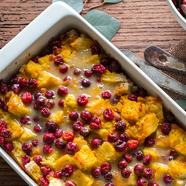 Baked pumpkin and cranberry bread pudding in a white baking dish, rustic wood backdrop.