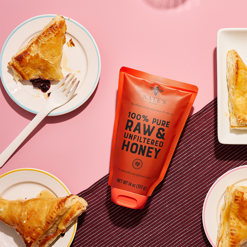 Turnovers on a plate, a pouch of Nate's Honey and turnovers on smaller plates, all on a pink surface. 