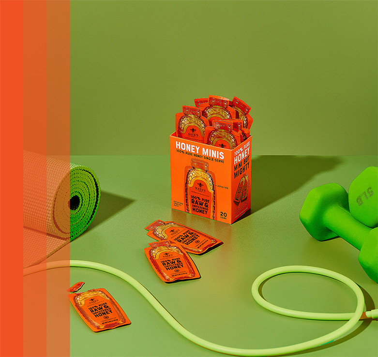 Box of Nate’s Organic Honey Minis surrounded by workout essentials like a yoga mat, dumbbells, and jump rope.