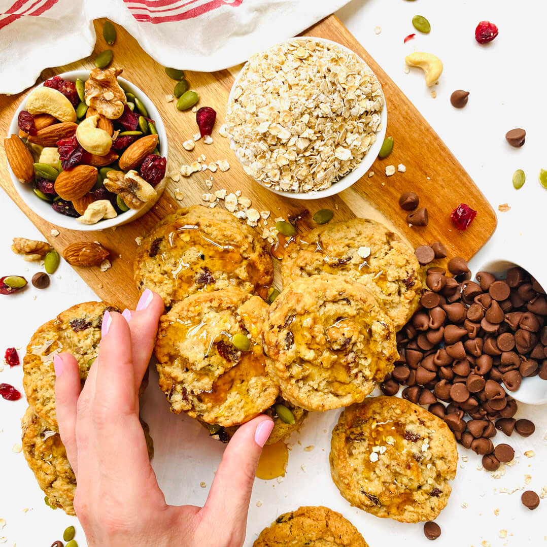 Hand grabbing cookie with scattered ingredients on wood platter with white background