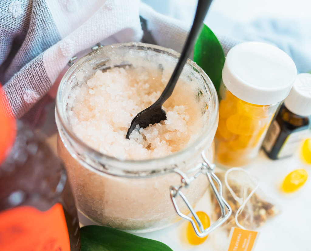 A jar of honey facial scrub with a spoon, essential oils and wellness supplements nearby.
