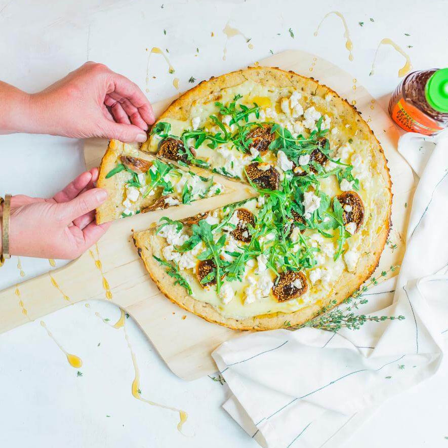 hands grabbing slice of flatbread next to bottle of Nate's organic honey on white background