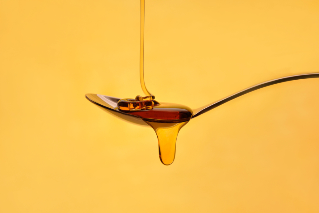 Golden honey drizzling off a spoon against a yellow background.