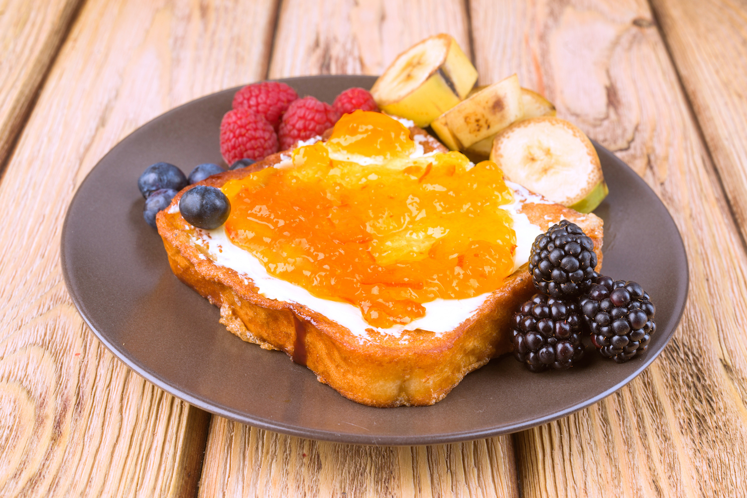 French toast with fruit and crystallized honey on a plate, wooden table background.
