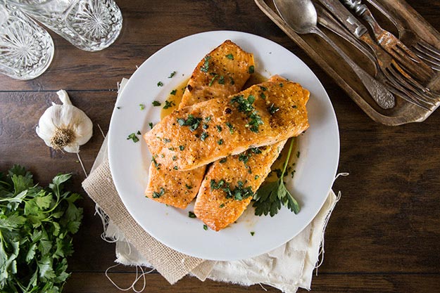Seared salmon fillets garnished with parsley on a white plate, rustic table setting.