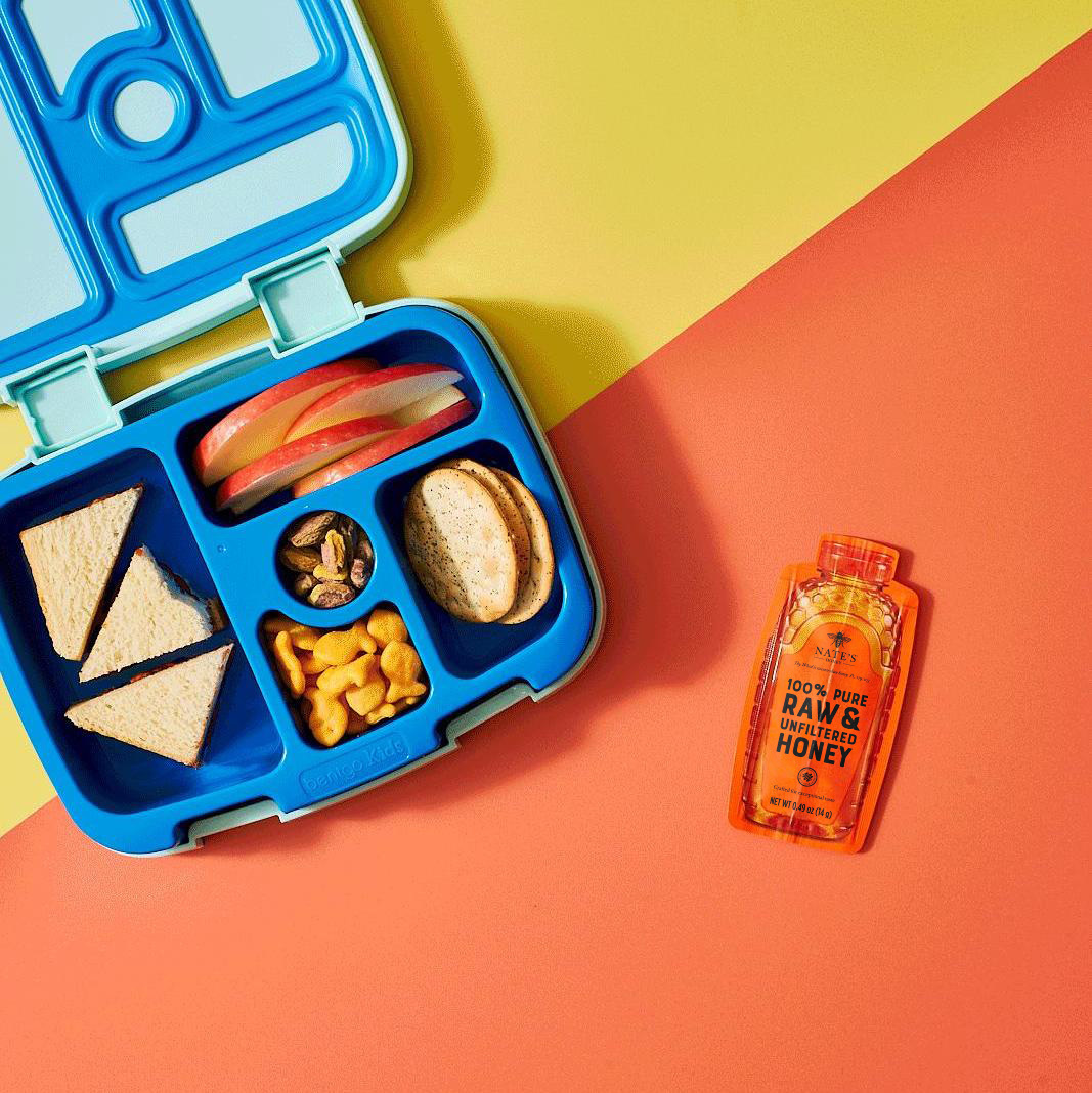 A blue lunchbox with sandwiches, apple slices, pretzels, and goldfish crackers, paired with Nate's Honey Minis.