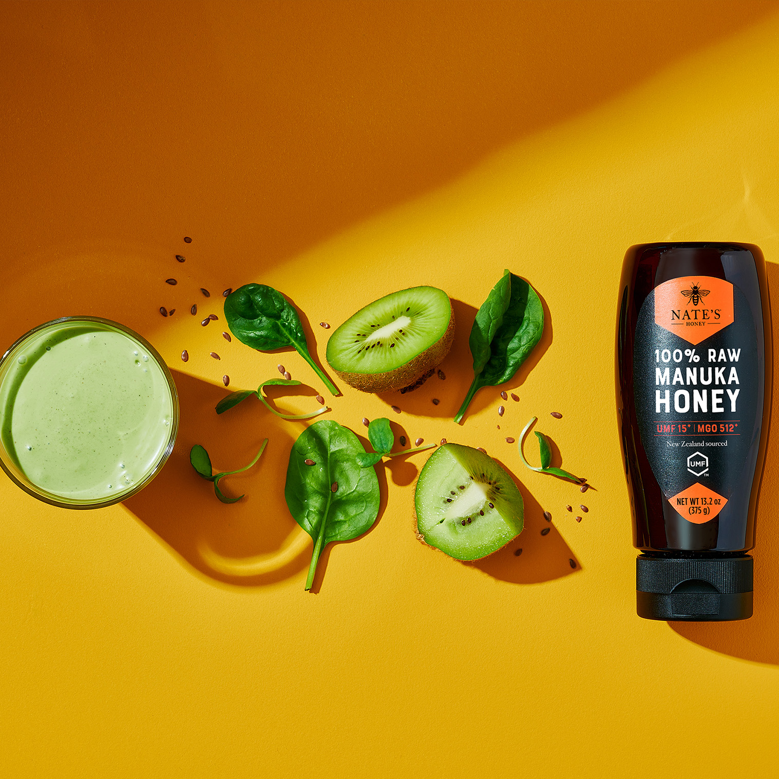 Manuka honey bottle next to a green smoothie on a yellow background.