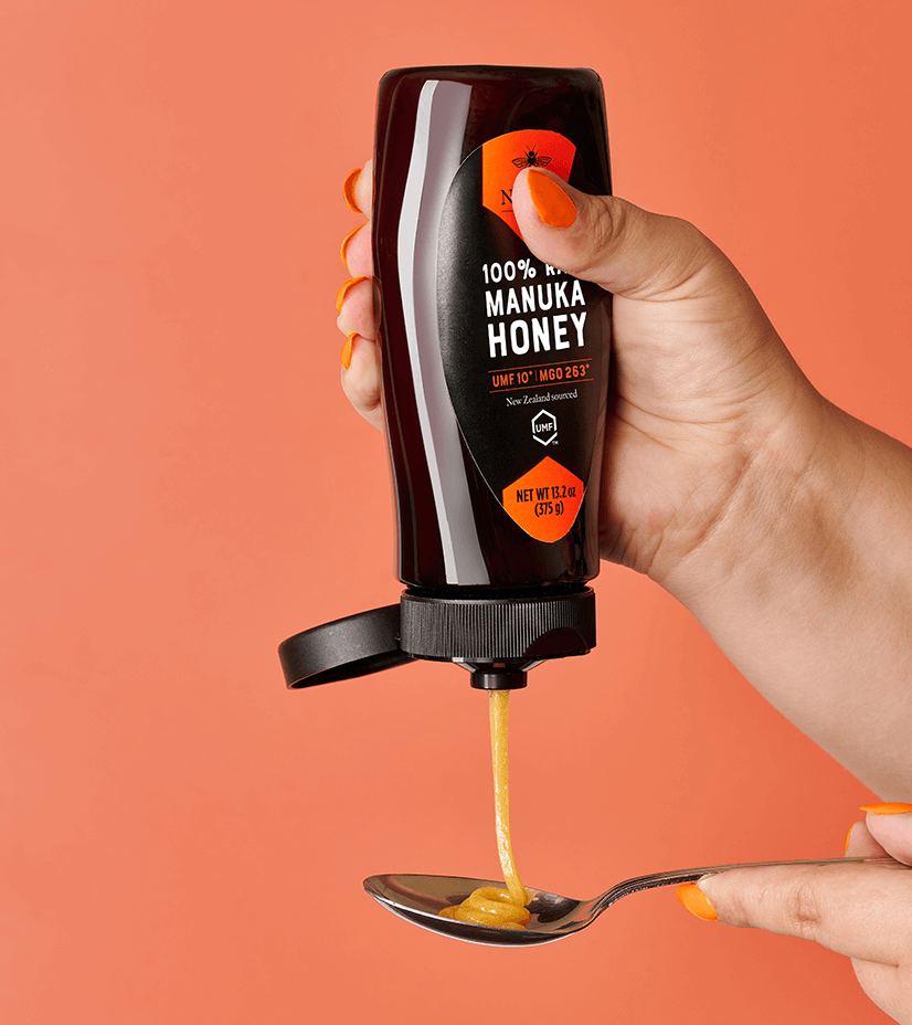 Manuka bottle being squeezed onto spoon with pink background.