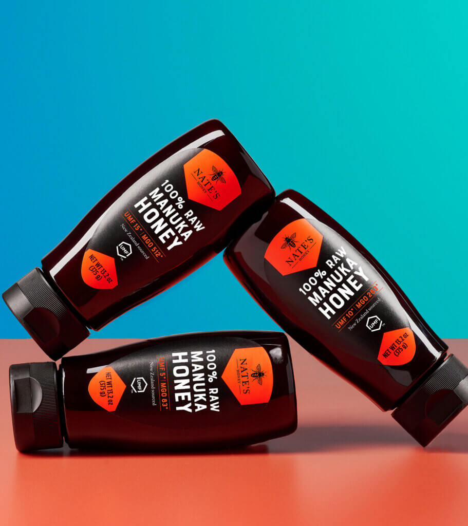 3 bottles of Manuka honey sitting on red table with blue backdrop