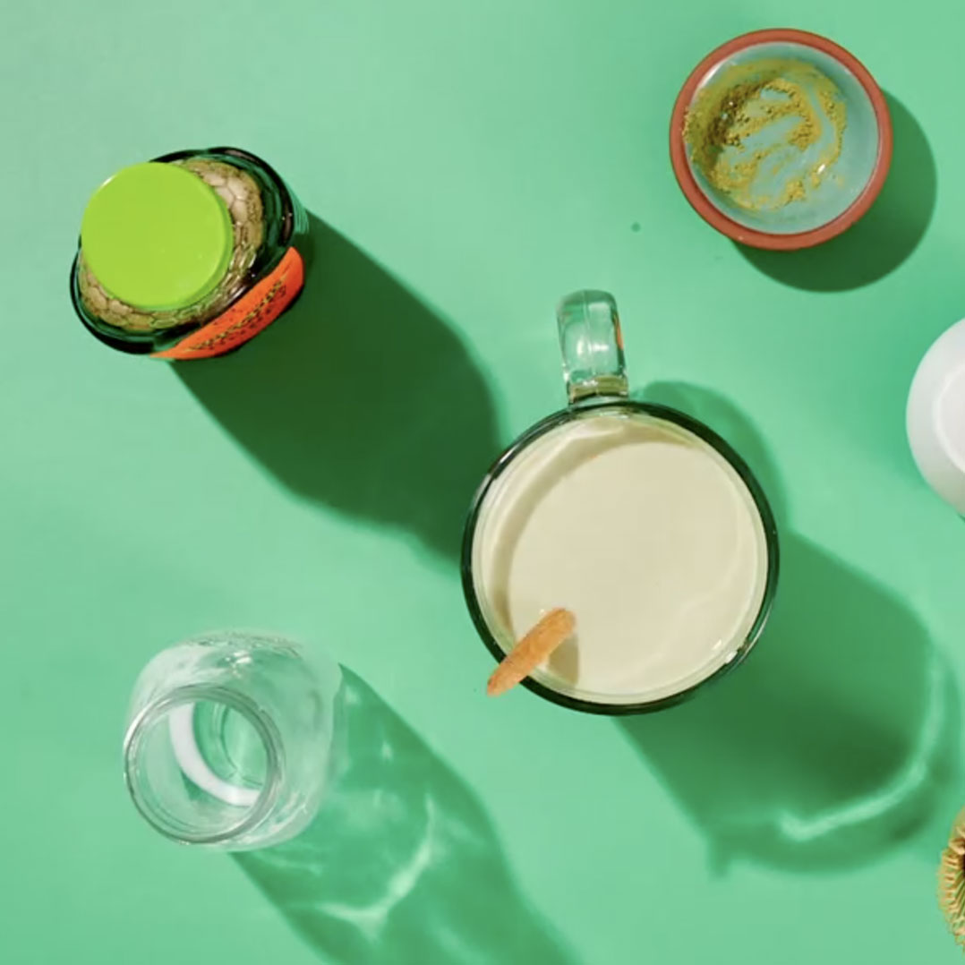 top view of Nate's Organic Honey and glasses with matcha latte ingredients on green background