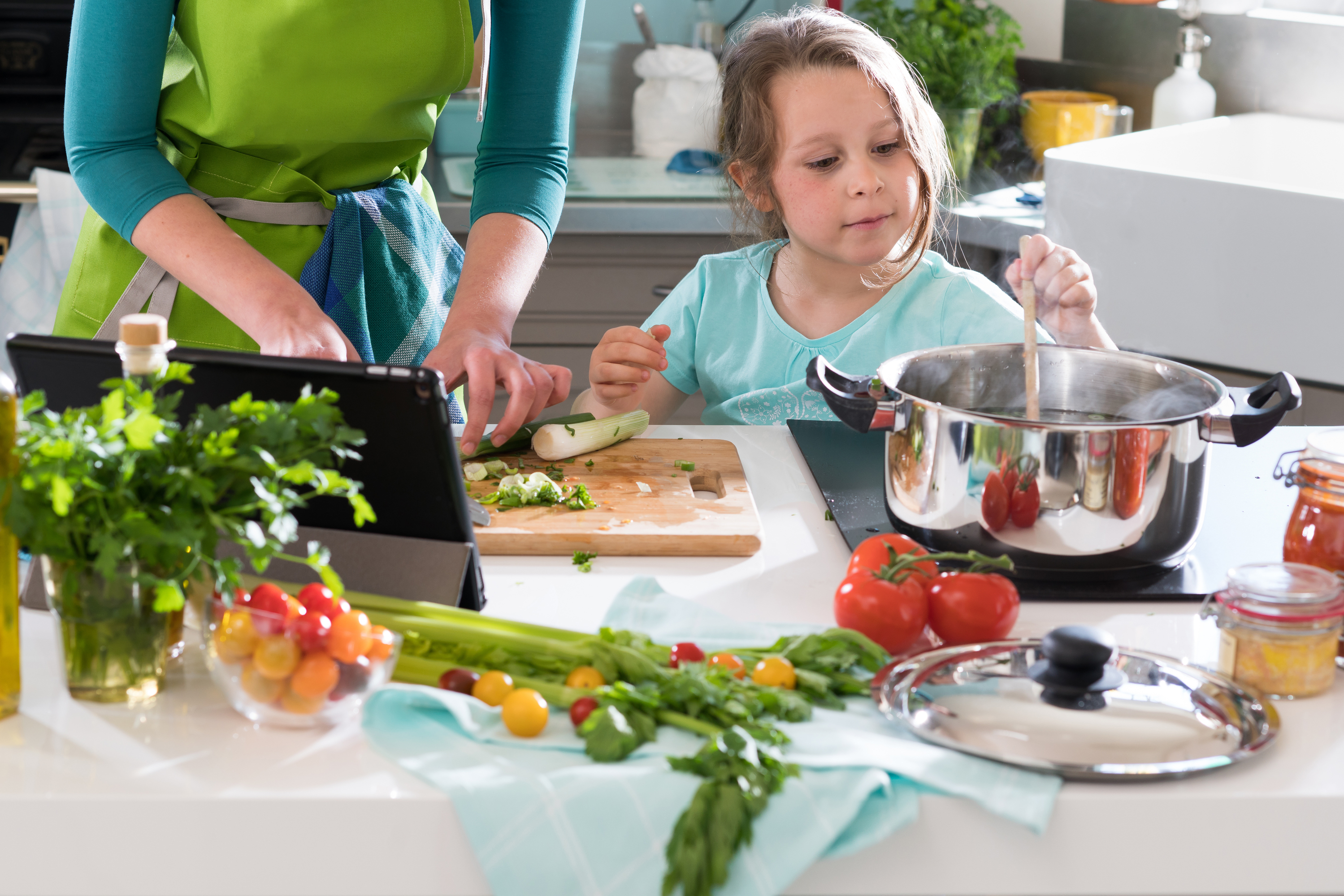 Adult and child cooking together with fresh ingredients in a bright kitchen.