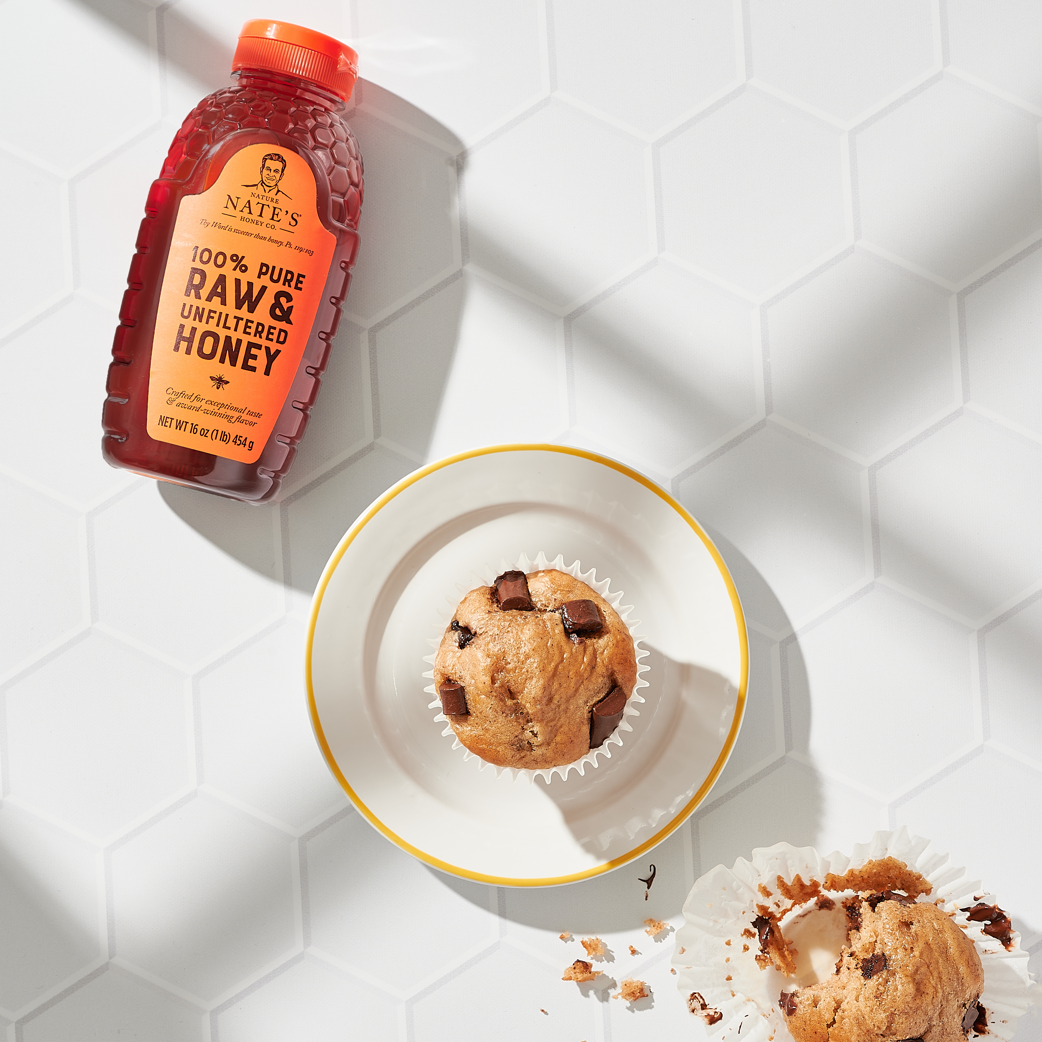 White plate holding a honey banana muffin next with a bottle of Nate's classic honey.