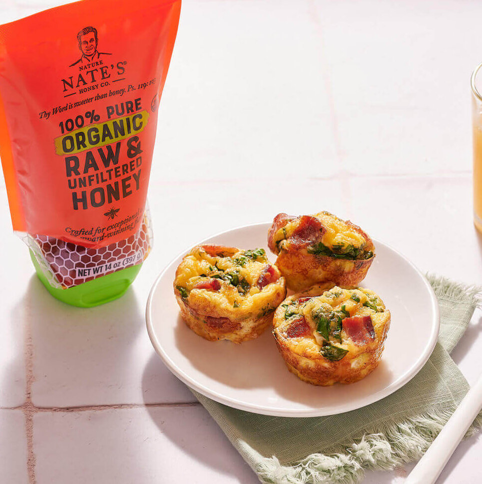 On a sunlit table, egg bites rest on a plate beside a pouch of Nate’s organic honey with toast and orange juice nearby.