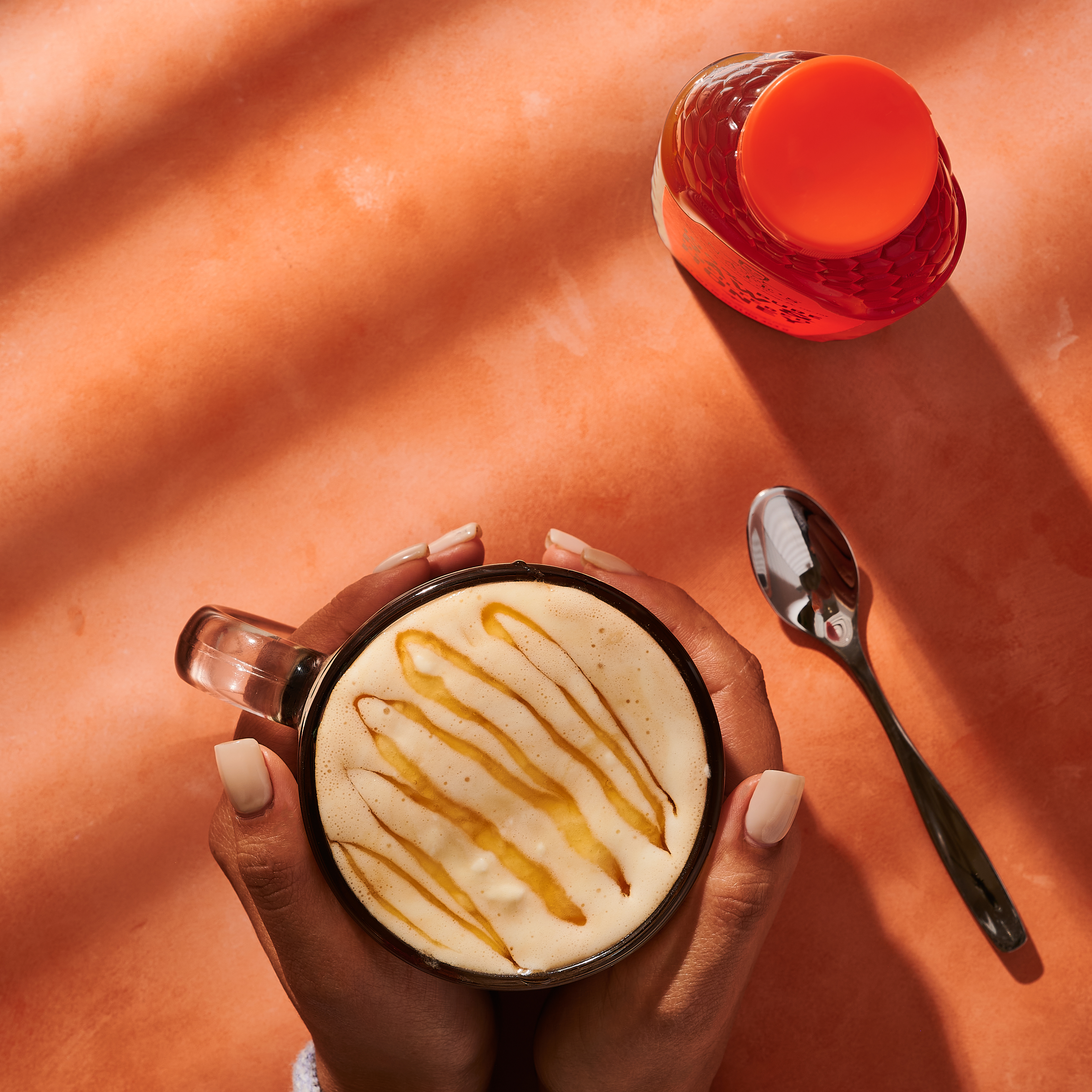 Hands holding a coffee mug drizzles with Nate's honey.