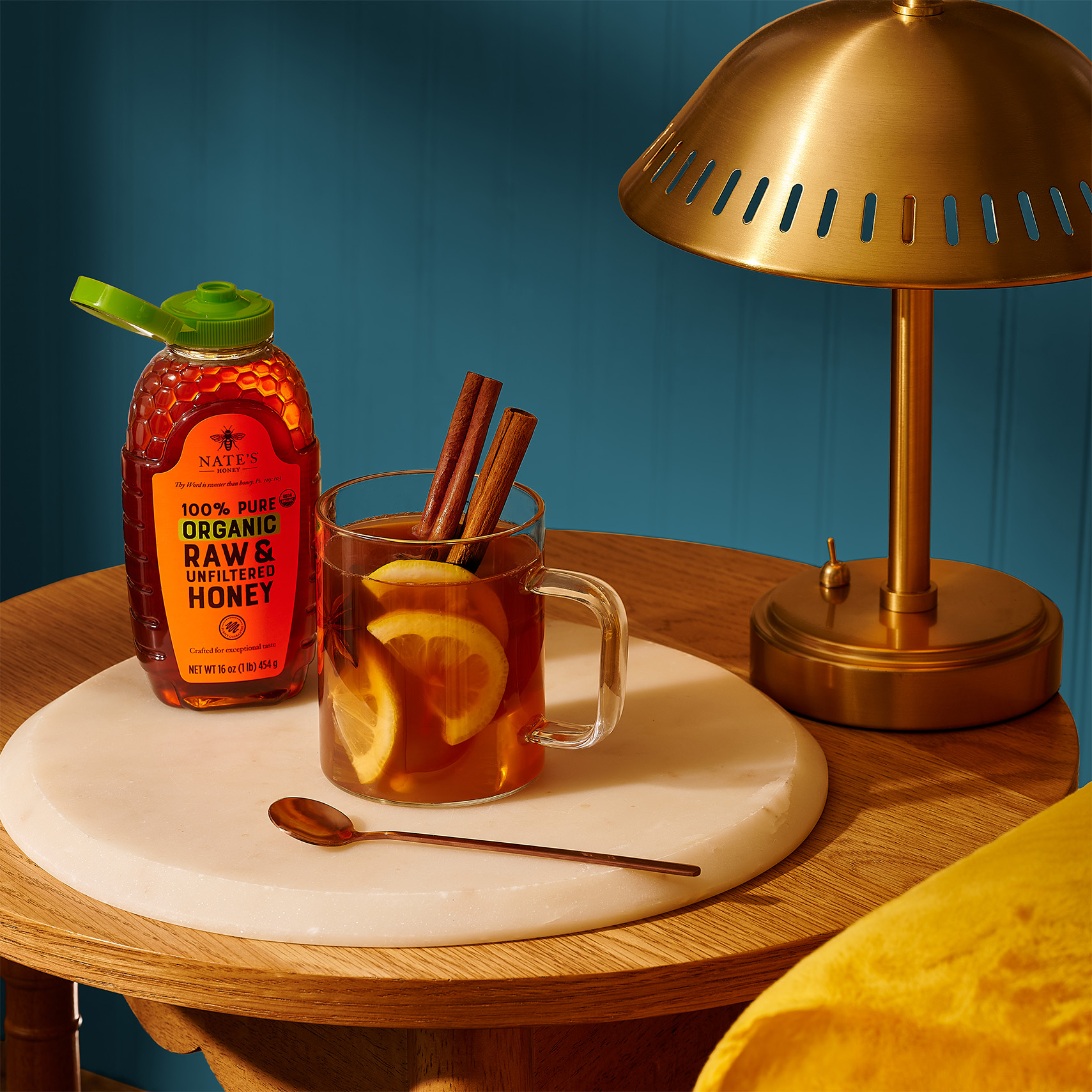 Bottle of organic honey beside a warm mug of tea with cinnamon on a wooden table.