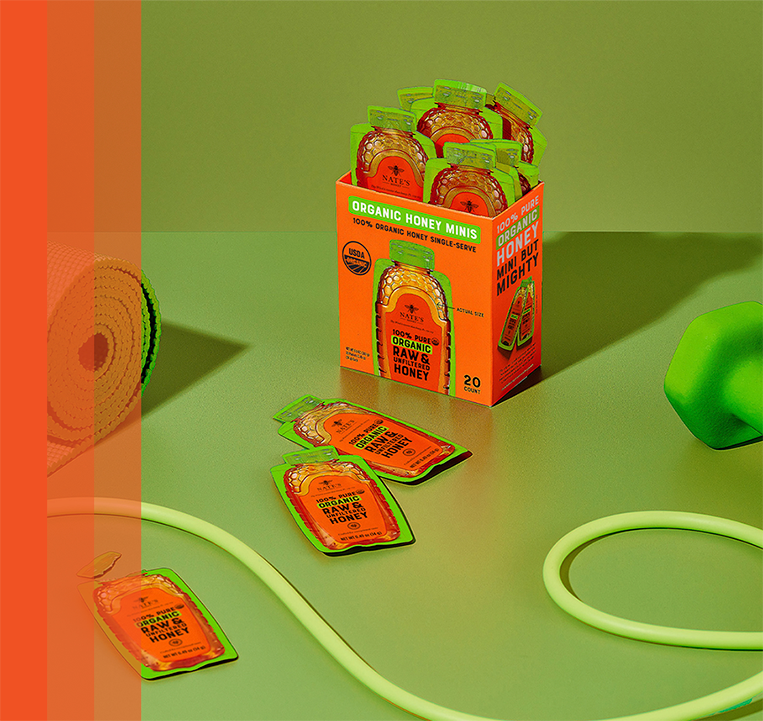 Box of Nate’s Organic Honey Minis surrounded by workout essentials like a yoga mat, dumbbells, and jump rope.