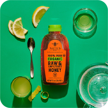 Organic bottle of honey on green background surrounded by tea, lemon slices and a clear mug.