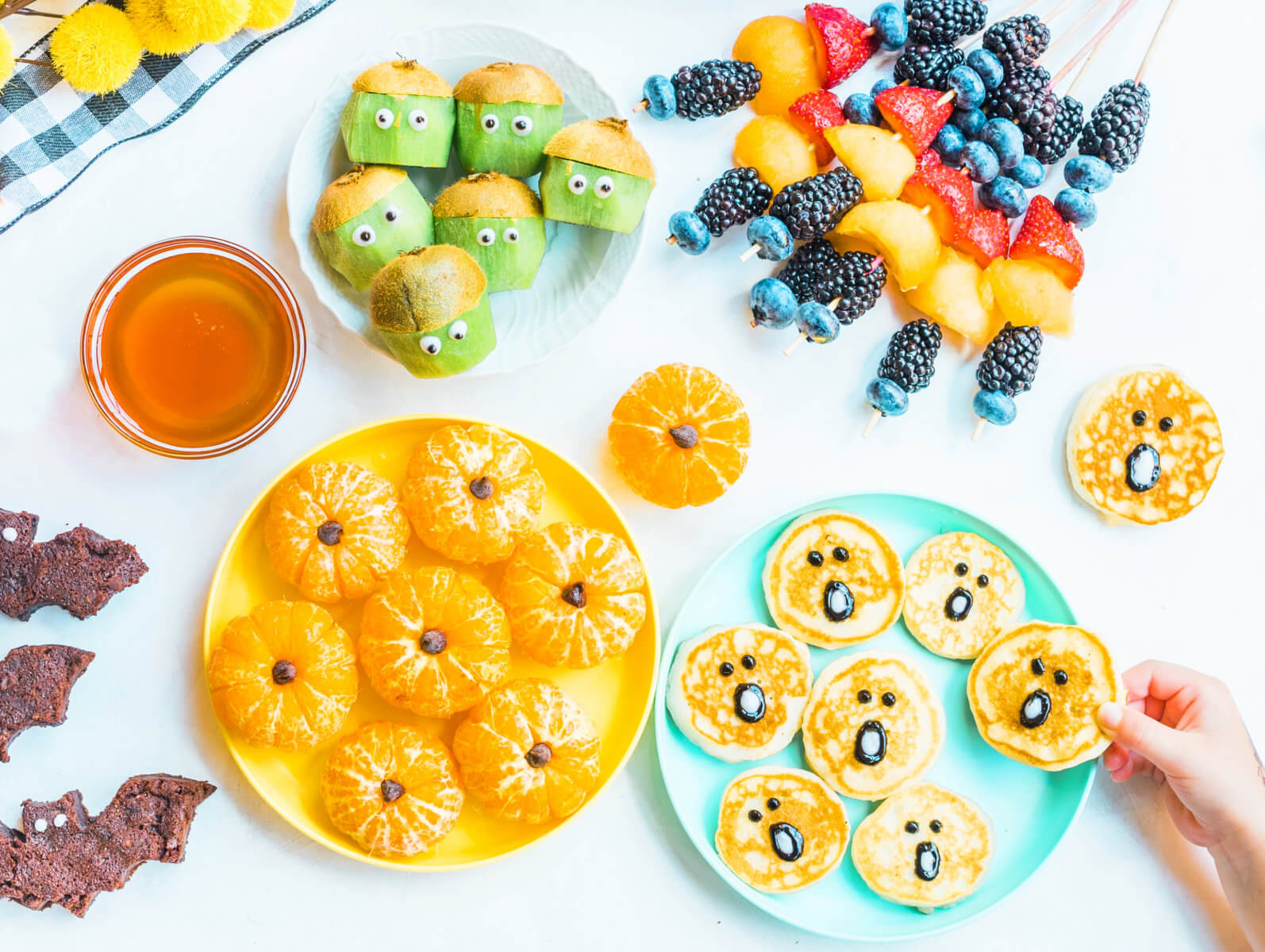A colorful snack spread with fruit, crackers, and a bowl of honey, crafted into playful, kid-friendly shapes.