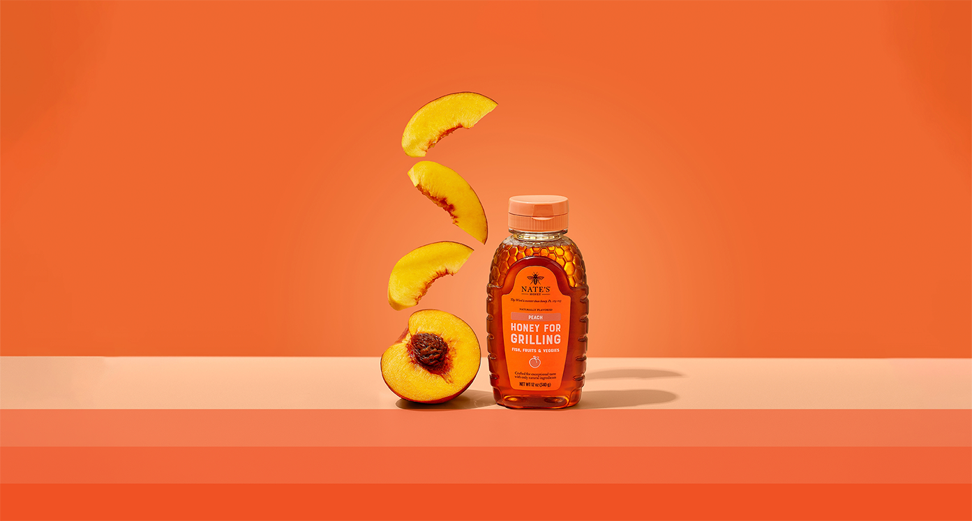 Nate's Peach Honey next to a halved peach and peach slices on orange background.