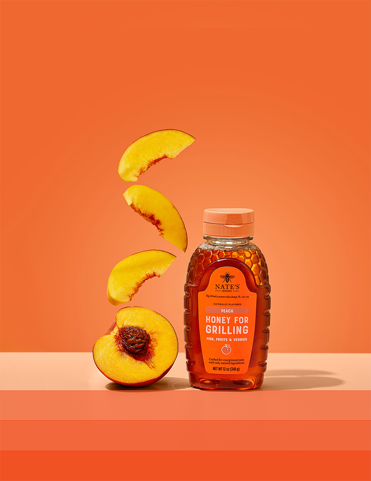 Nate's Peach Honey next to a halved peach and peach slices on orange background.
