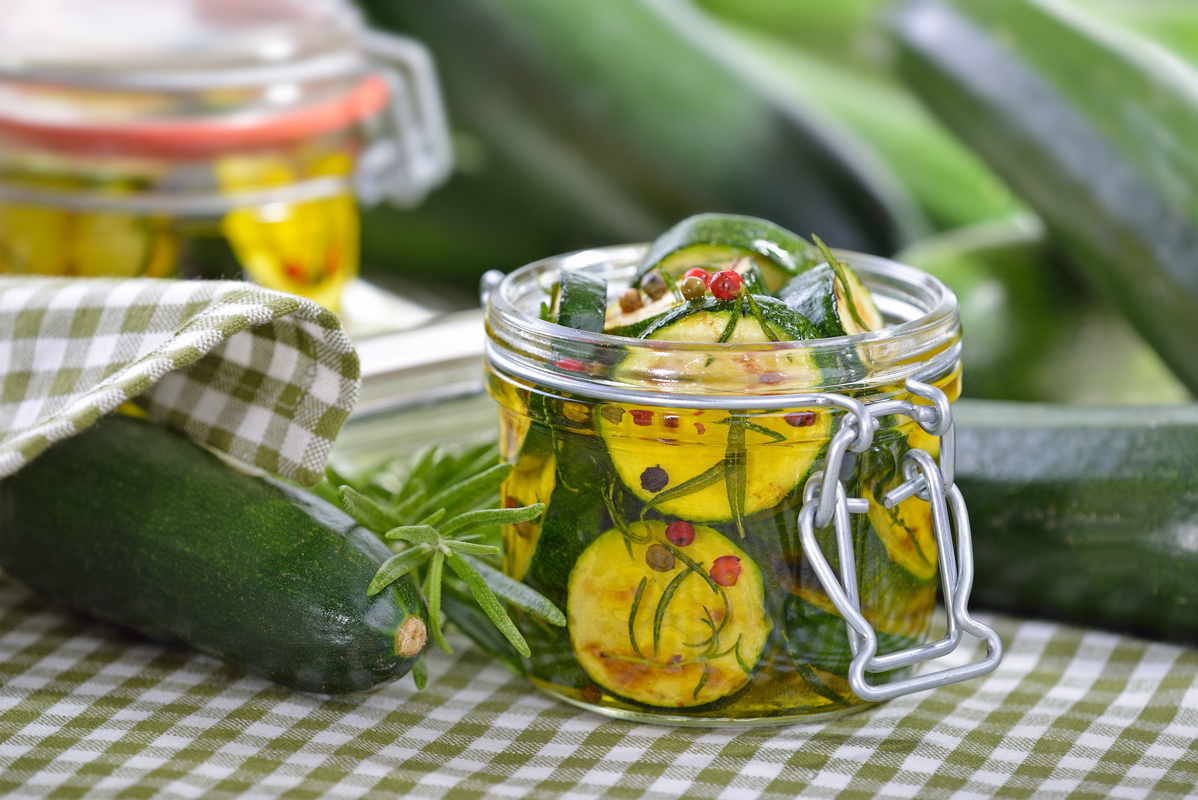 Jar of pickled cucumbers on a checkered cloth with fresh herbs, embodying home-canned goodness.