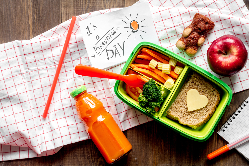Healthy lunchbox, juice, and It's Earth Day, drawing on a wooden table.