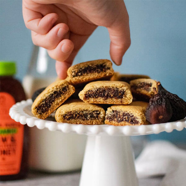 A hand reaching for homemade Fig Newtons from a white platter