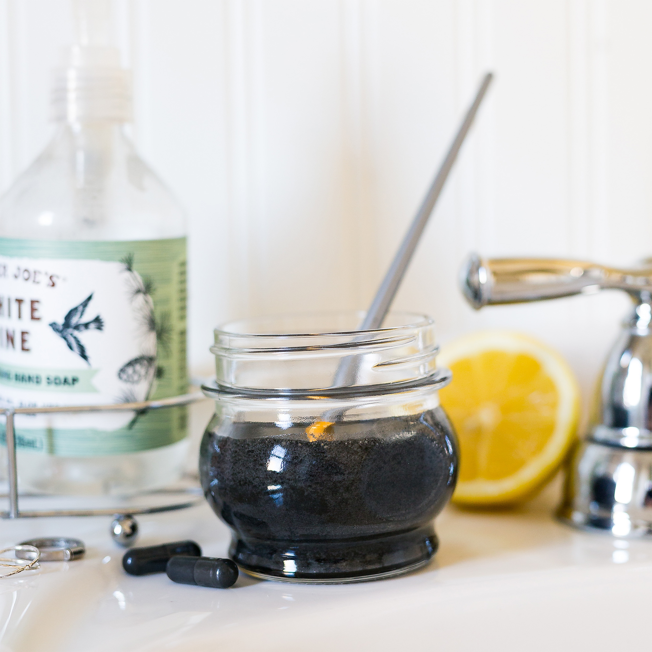 Jar of a homemade honey scrub styled beside a sink with lemon and simple skincare ingredients.