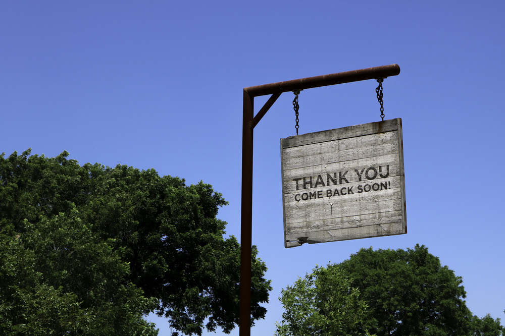 Rustic Thank You Come Back Soon sign against a blue sky with trees. Rustic Thank You Come Back Soon sign against a blue sky with trees.