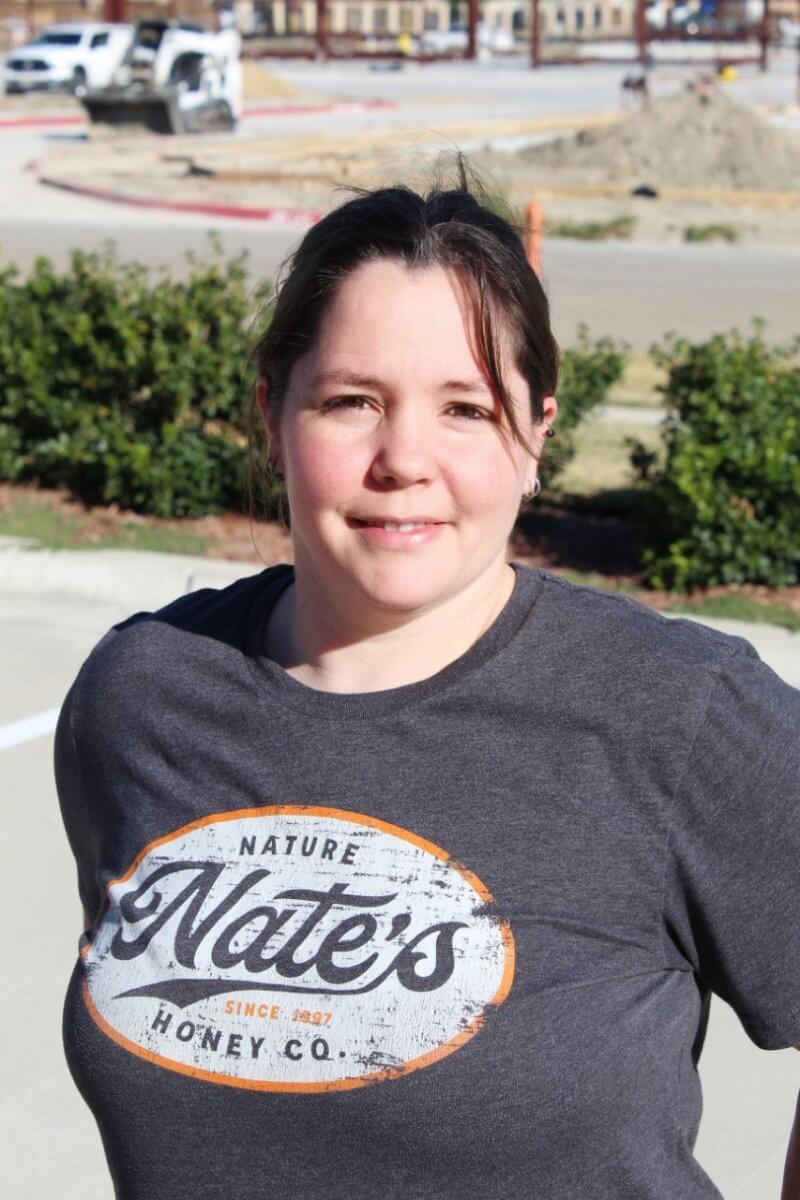 An employee wearing a Nate's Honey Co. t-shirt standing outside with a street and construction in the background.