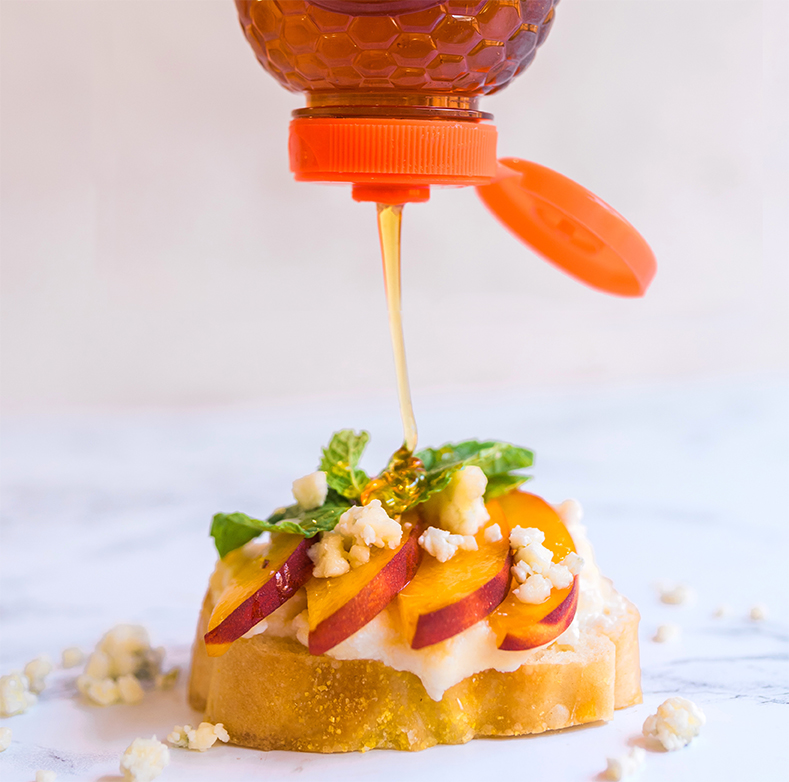 Open Nate's honey bottle pouring on peach and cheese toast.