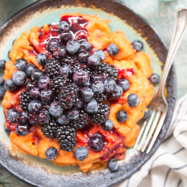 Sweet potato waffles topped with berries on a plate beside a striped napkin.