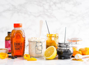 Vibrant Nate's honey bottle with homemade honey scrubs in jars on marble with citrus peels.