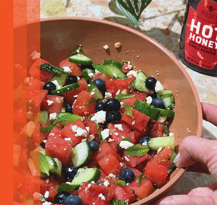 Bol de ensalada de sandía con pepino, arándanos, queso feta y menta, rociada con miel picante.